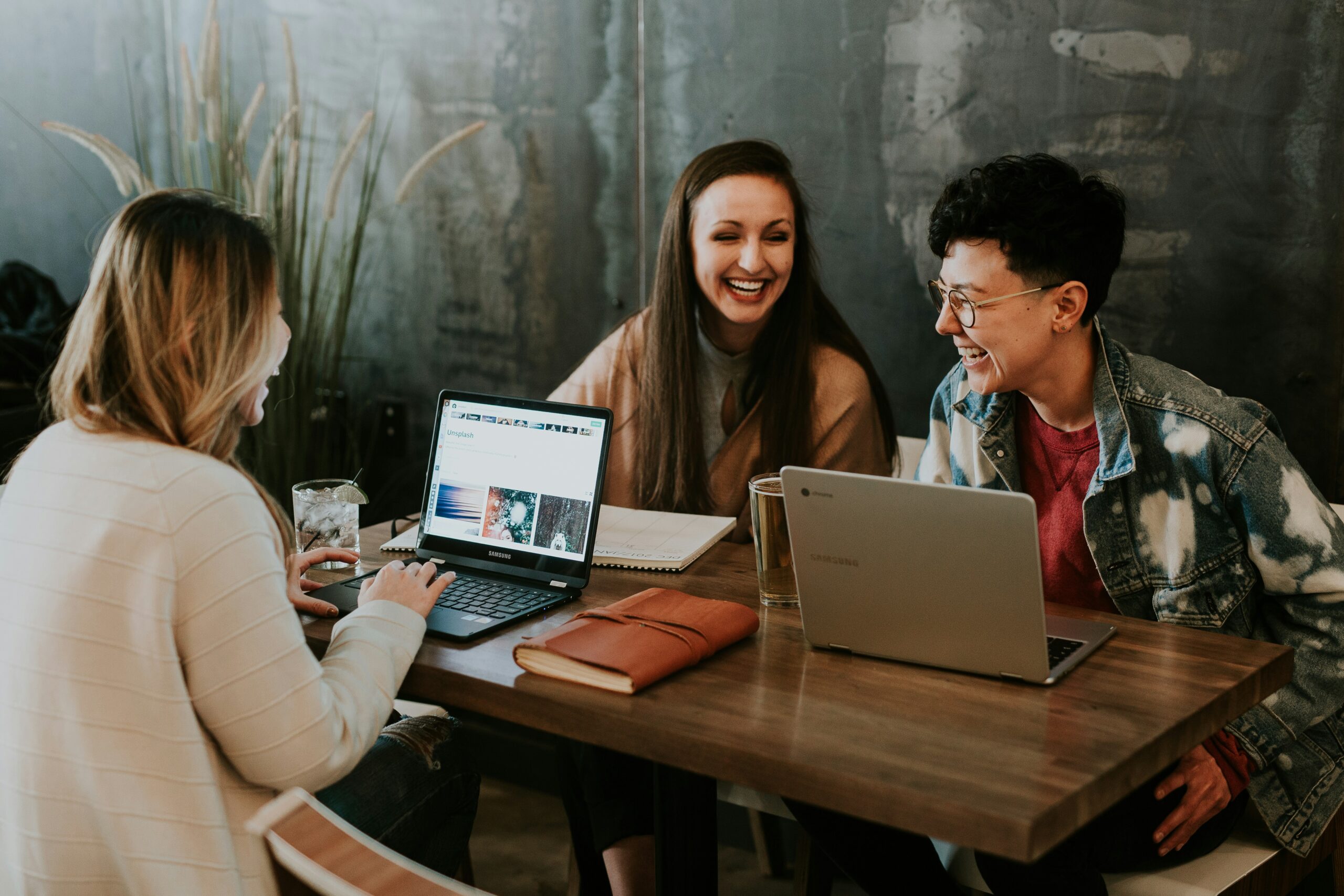 A group of diverse employees laughing and collaborating around a laptop in a modern office.